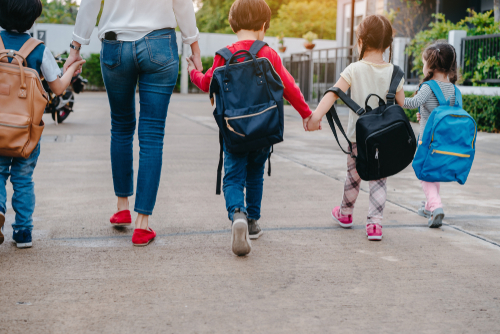 back view of kids holding hands with a grown woman going to school